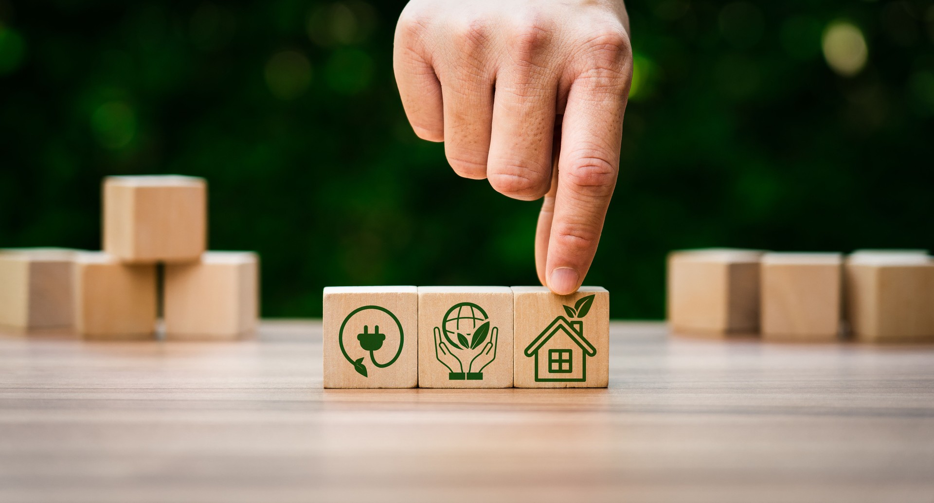 Hand Arranging Wooden Blocks with Green Sustainable Icons Representing Renewable Energy, Environmental Protection, and Eco-Friendly Housing for Sustainable Living